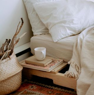 Comfortable cozy bedroom with bed wooden shelves with book and cup while wicker basket with sticks placed on ethnic styled rug