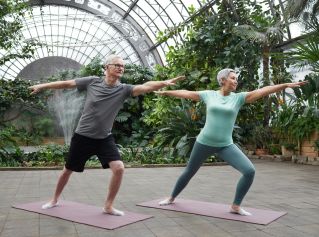 Elderly couple enjoying yoga exercises together in a lush greenhouse setting.