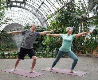 Elderly couple enjoying yoga exercises together in a lush greenhouse setting.